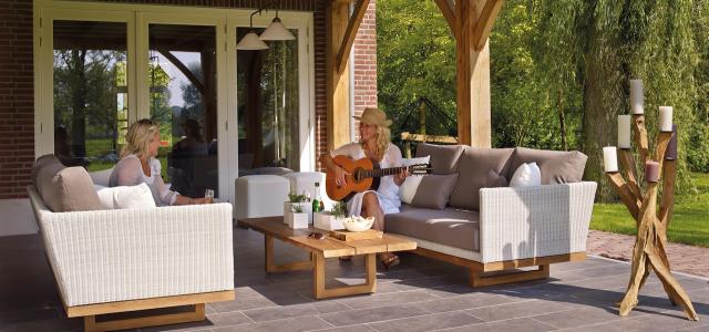 Two women sitting outside on a patio. One woman is playing guitar, and the other is listening and smiling.